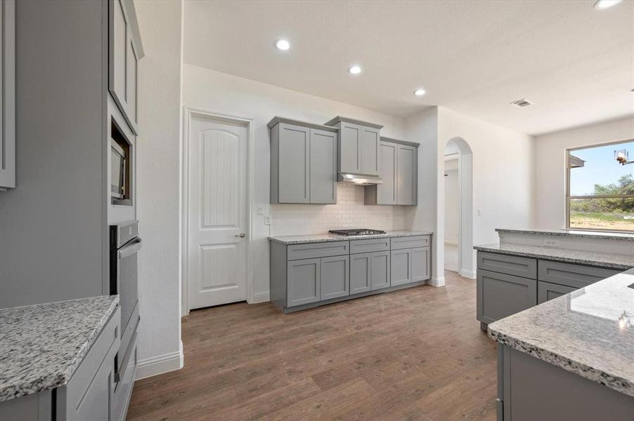 Kitchen with tasteful backsplash, dark hardwood / wood-style flooring, appliances with stainless steel finishes, gray cabinetry, and light stone counters