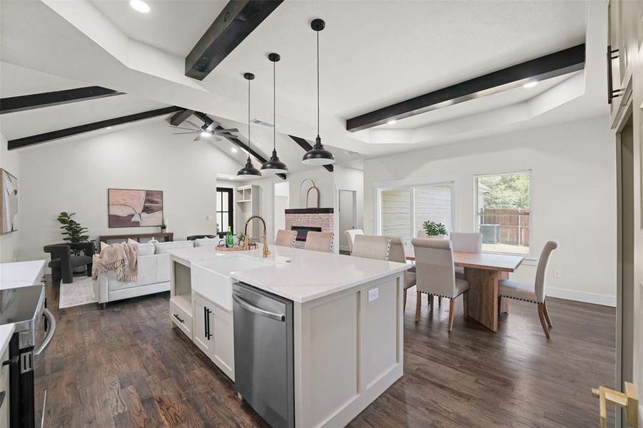 Open-concept living space featuring wood-finish flooring, a kitchen island with a farmhouse sink and pendant lighting, a vaulted ceiling with exposed beams, and a dining area with direct outdoor access Open-concept living space featuring wood-finish flooring, a kitchen island with a farmhouse sink and pendant lighting, a vaulted ceiling with exposed beams, and a dining area with direct outdoor access