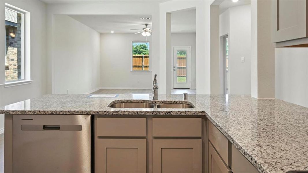 Kitchen featuring light stone counters, dishwasher, gray cabinetry, open floor plan, and a ceiling fan