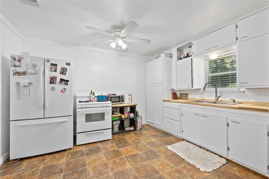 Kitchen featuring white appliances, stone finish flooring, ceiling fan, white cabinetry, and ornamental molding Kitchen featuring white appliances, stone finish flooring, ceiling fan, white cabinetry, and ornamental molding