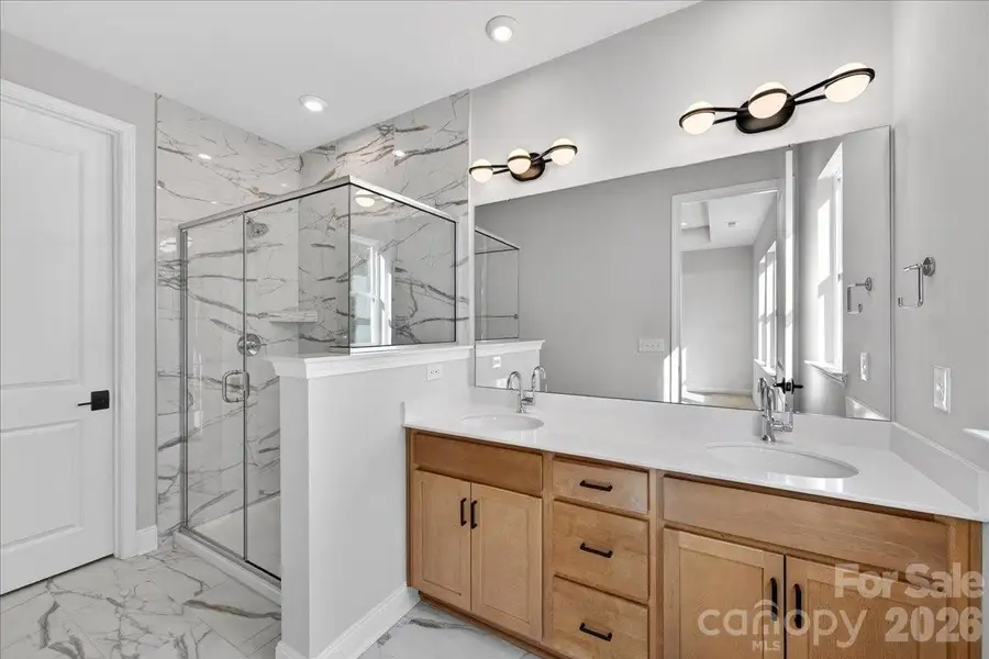 Dual vanity primary bathroom with warm brown cabinets