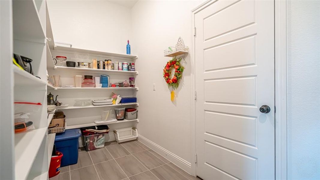 Corner pantry featuring expansive shelving, light gray tile flooring, and a white paneled door
