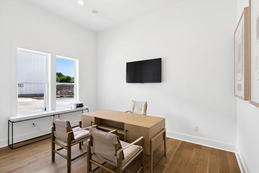 Light-filled interior space featuring wood-finish flooring, white walls, recessed lighting, and a window sill with a minimalist metal frame