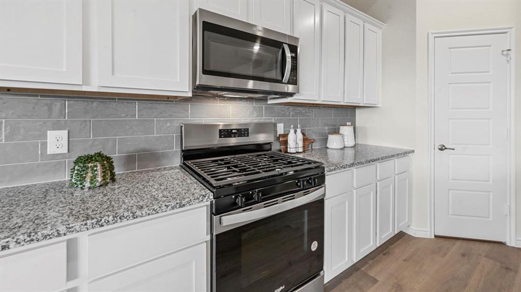 Kitchen featuring stainless steel appliances, white cabinetry, dark wood-style flooring, light stone countertops, and tasteful backsplash