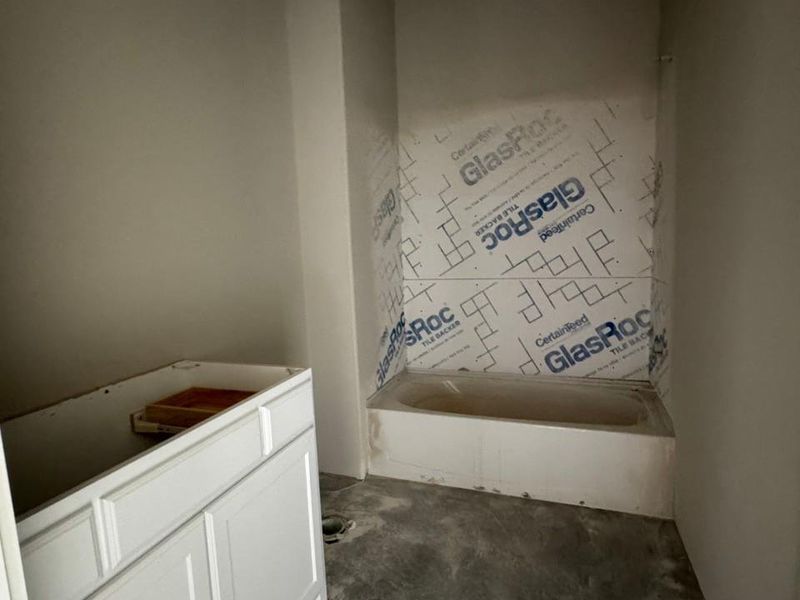 Bathroom under construction featuring a white tub, tile backer board, and a white vanity base awaiting installation