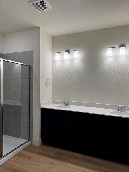 Full bath with wood finished floors, a shower stall, double vanity, and a textured ceiling Full bath with wood finished floors, a shower stall, double vanity, and a textured ceiling