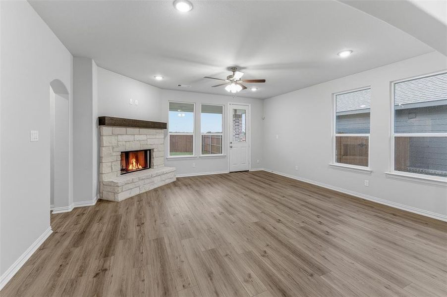 Spacious living area featuring wood-finish flooring, a stone fireplace with a substantial mantel, a ceiling fan, recessed lighting, and multiple windows Spacious living area featuring wood-finish flooring, a stone fireplace with a substantial mantel, a ceiling fan, recessed lighting, and multiple windows