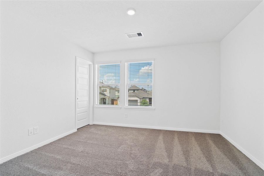 This secondary bedroom offers comfort and style with plush carpeting, neutral paint tones, recessed lighting, large windows with blinds, and a walk-in closet.