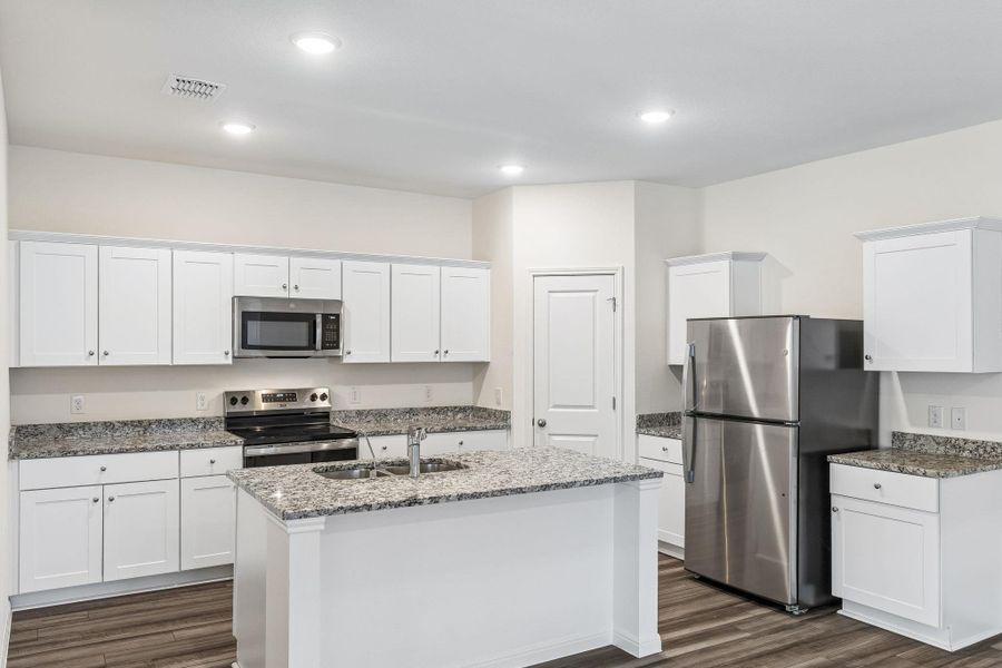 Kitchen with stainless steel appliances, white cabinets, an island with sink, dark wood-style flooring, and dark stone countertops