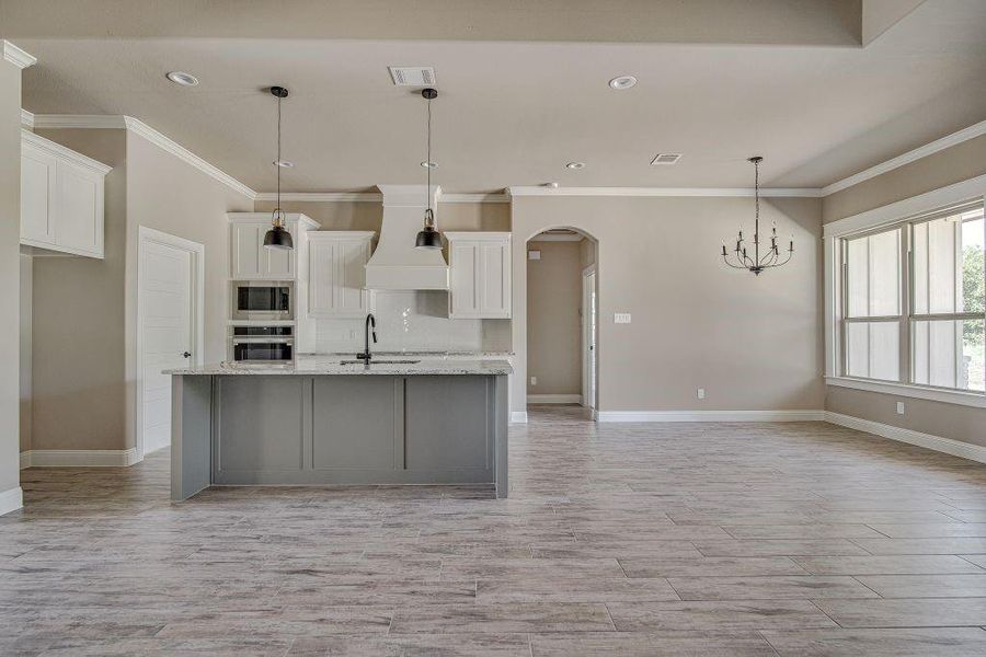 Kitchen with decorative light fixtures, premium range hood, an island with sink, appliances with stainless steel finishes, and white cabinets