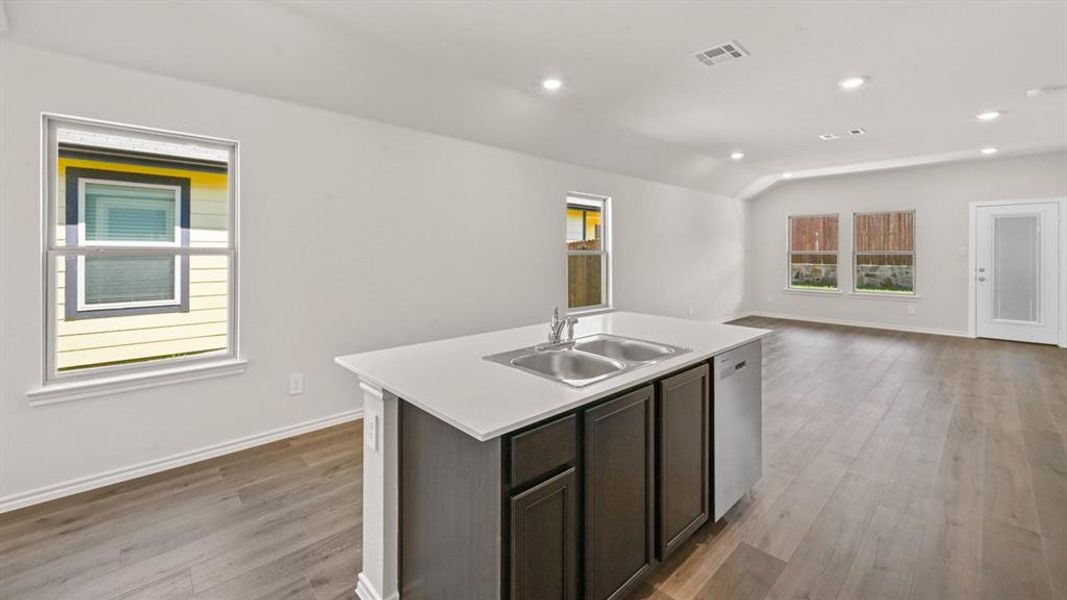 Kitchen island with an undermount double-basin stainless steel sink, solid surface countertop, and dark wood cabinetry
