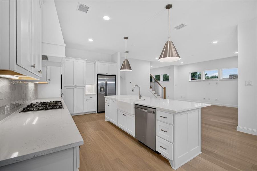 Modern kitchen featuring white shaker cabinetry, stainless steel appliances, a center island with farmhouse sink, wood-finish flooring, and recessed lighting Modern kitchen featuring white shaker cabinetry, stainless steel appliances, a center island with farmhouse sink, wood-finish flooring, and recessed lighting