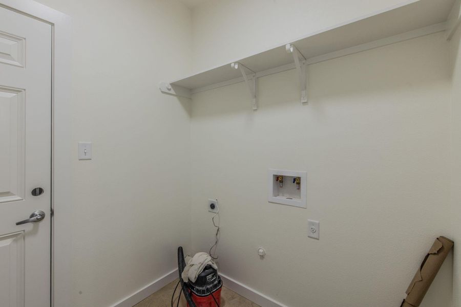 Dedicated laundry area featuring a white wall shelf, built-in plumbing connections, and a light-toned flooring Dedicated laundry area featuring a white wall shelf, built-in plumbing connections, and a light-toned flooring