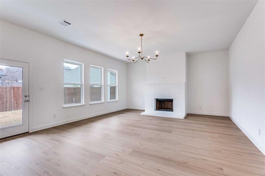 Unfurnished living room featuring a brick fireplace, a chandelier, and light wood-type flooring