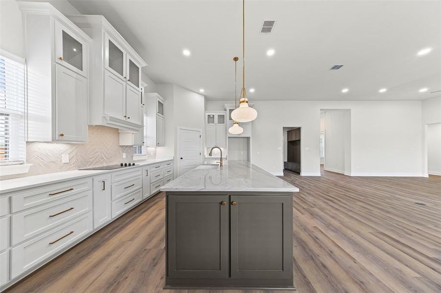 Kitchen with white cabinets, glass insert cabinets, a center island with sink, light stone countertops, and recessed lighting Kitchen with white cabinets, glass insert cabinets, a center island with sink, light stone countertops, and recessed lighting