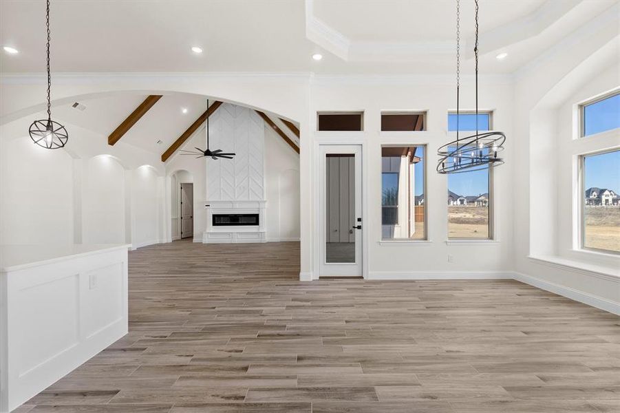 Breakfast room and view to living room with ceiling fan with notable chandelier, crown molding, lofted ceiling with beams, and a fireplace