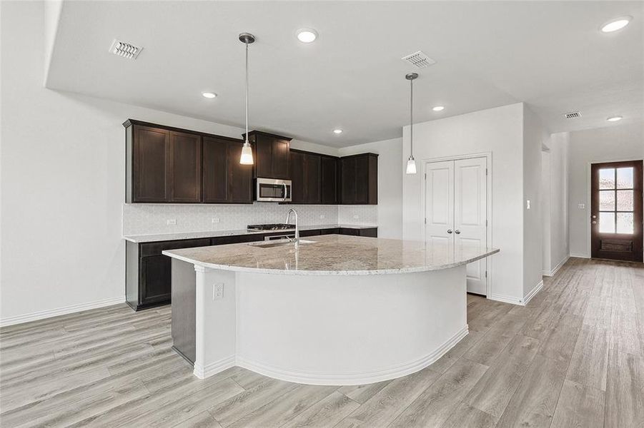 Kitchen featuring backsplash, light wood-type flooring, light stone countertops, and an island with sink