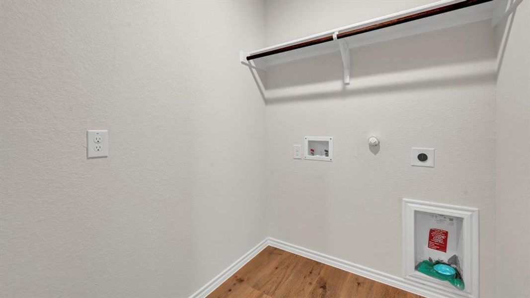 Dedicated laundry space featuring wood-finish flooring, white baseboards, and light-toned walls