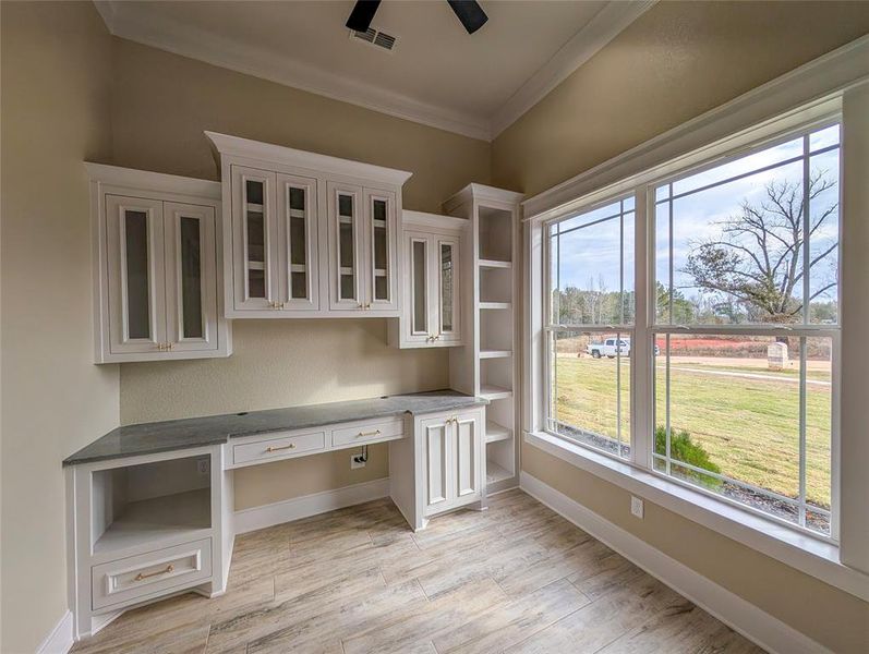 Unfurnished office featuring built in desk, crown molding, and wood tiled floors