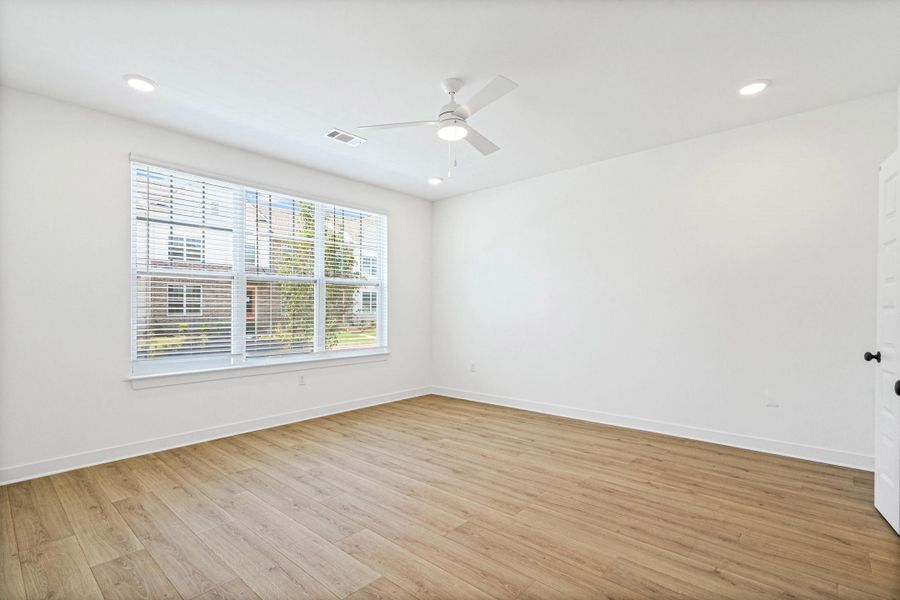 Spacious room featuring wood-finish flooring, a large window with horizontal blinds, a ceiling fan with integrated lighting, and recessed ceiling lights Spacious room featuring wood-finish flooring, a large window with horizontal blinds, a ceiling fan with integrated lighting, and recessed ceiling lights