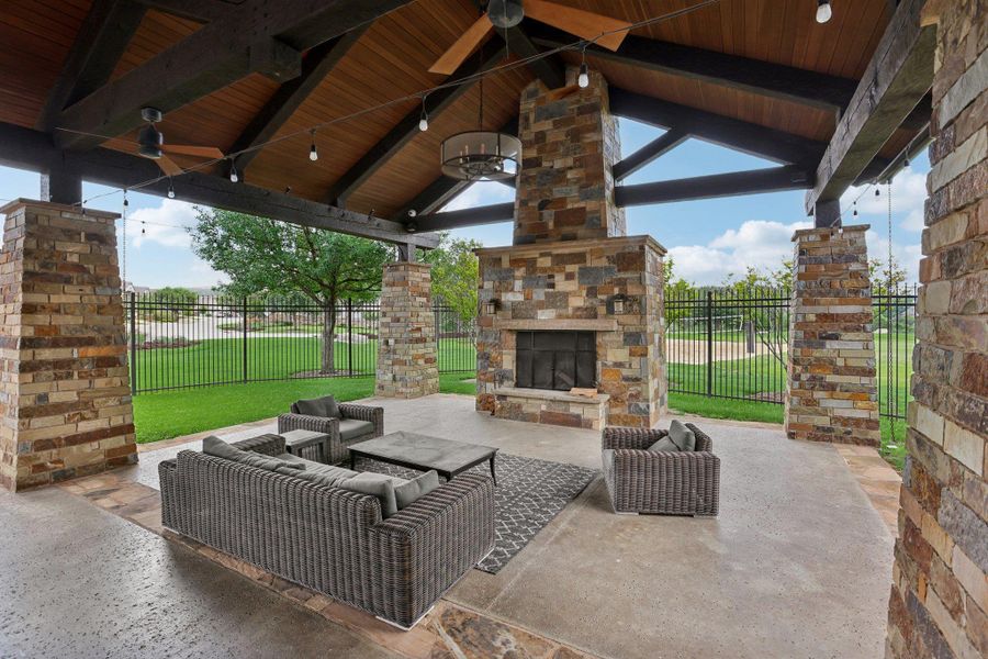Expansive covered outdoor living area featuring a stone fireplace, exposed wooden beams, and a wood plank ceiling