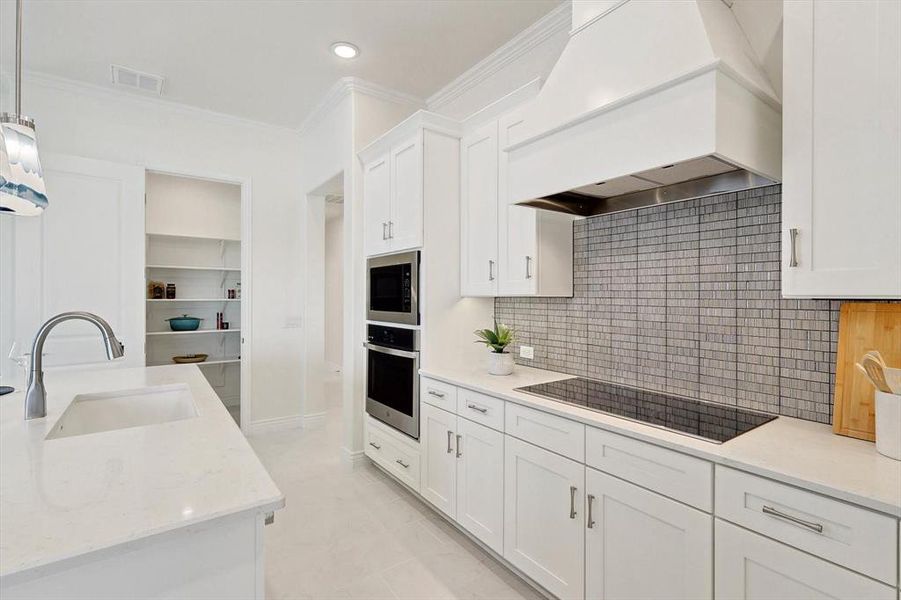 Kitchen featuring tasteful backsplash, stainless steel appliances, premium range hood, light tile floors, and white cabinetry