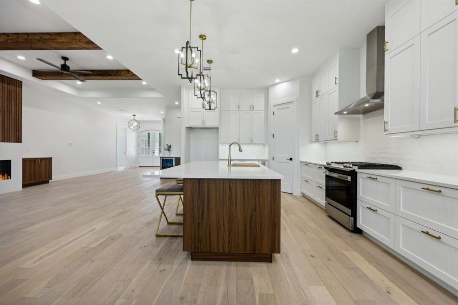 Kitchen with stainless steel gas stove, beamed ceiling, light wood-type flooring, and wall chimney range hood