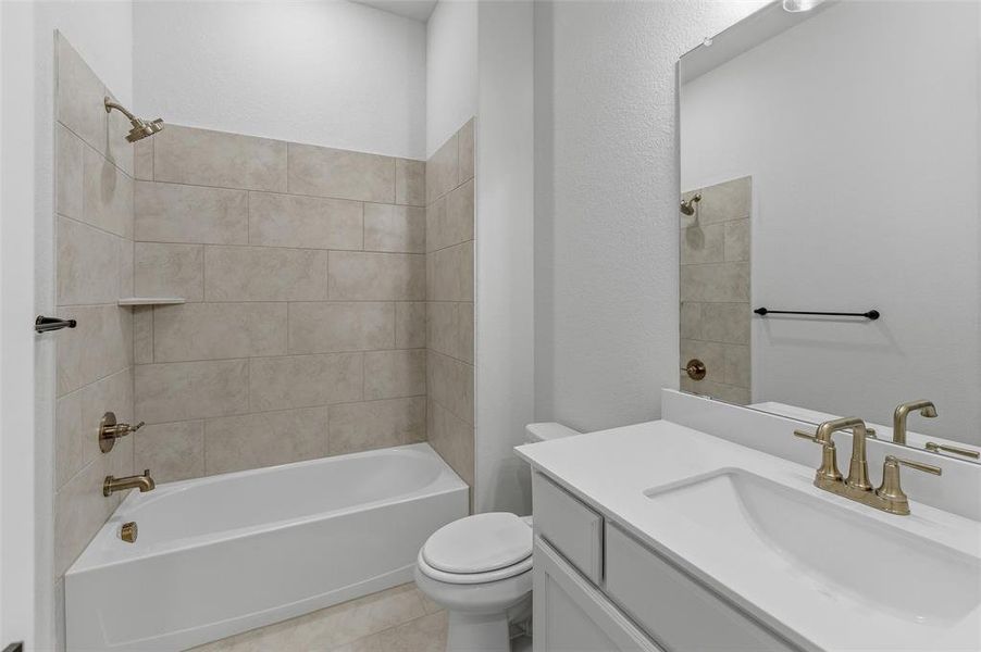 Bathroom featuring a built-in tub with tile surround, a single vanity with an integrated sink, a rectangular mirror, and bronze-finish fixtures Bathroom featuring a built-in tub with tile surround, a single vanity with an integrated sink, a rectangular mirror, and bronze-finish fixtures