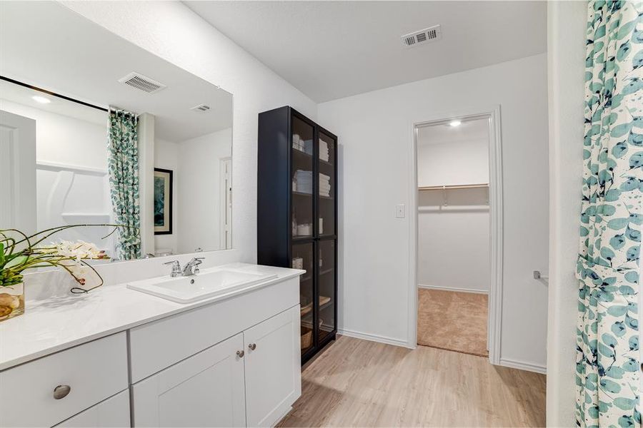 Bathroom with light wood finished floors, vanity, a walk in closet, and a shower with shower curtain Bathroom with light wood finished floors, vanity, a walk in closet, and a shower with shower curtain