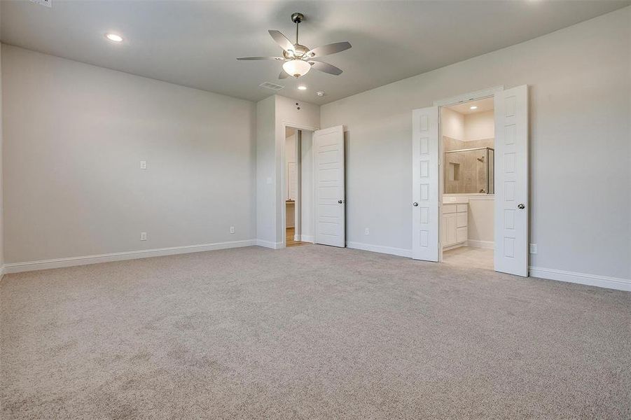 Unfurnished bedroom with light carpet, ensuite bathroom, and ceiling fan