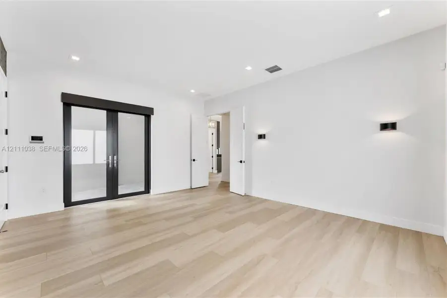 Room featuring light wood-finish flooring, recessed lighting, matte black wall-mounted fixtures, and glass-paned double doors with a dark frame