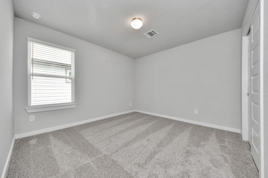 Secondary bedroom features plush carpeting, large windows that let in plenty of natural light, bright paint, and spacious closets. Sample photo of completed home with similar floor plan. Actual colors and selections may vary.