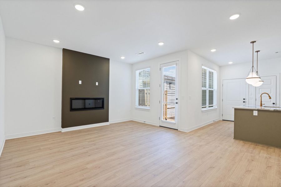 Open-concept living area featuring light wood-finish flooring, recessed lighting, and a contemporary fireplace with a dark accent wall Open-concept living area featuring light wood-finish flooring, recessed lighting, and a contemporary fireplace with a dark accent wall