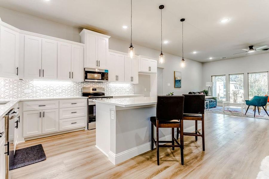 Kitchen with stainless steel appliances, ceiling fan, white cabinets, a kitchen island, and hanging light fixtures