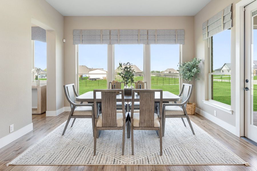 Dining room with wood table, six chairs, hardwood floors, and large windows overlooking a backyard