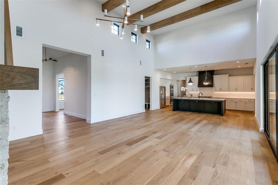 Unfurnished living room featuring light wood finished floors, beamed ceiling, and a high ceiling