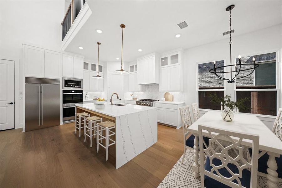 Kitchen featuring glass insert cabinets, white cabinets, built in appliances, light stone counters, and hanging light fixtures