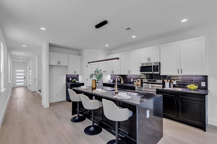 Kitchen with pendant lighting, a kitchen island with sink, white cabinets, sink, and appliances with stainless steel finishes