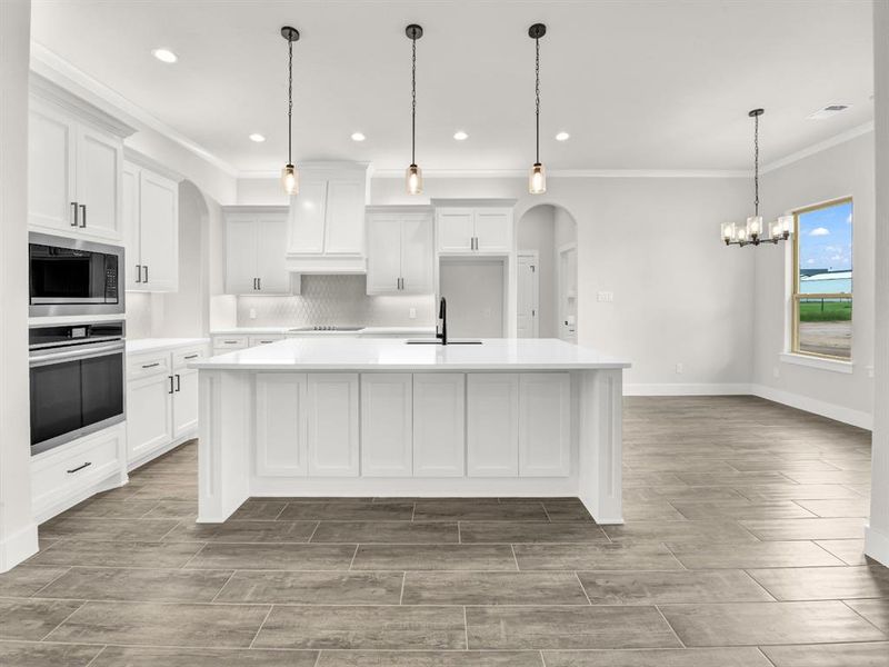 Kitchen with arched walkways, ornamental molding, a large island with sink, wood finish floors, and white cabinets