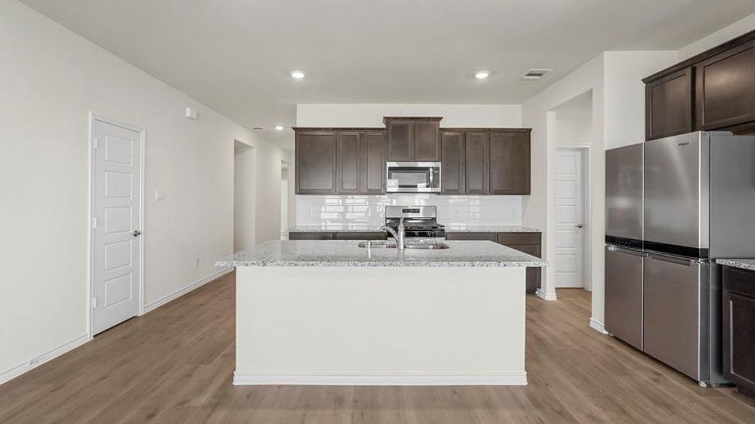 The kitchen features a central island with a sink, dark wood cabinetry, stainless steel appliances, and light-colored countertops