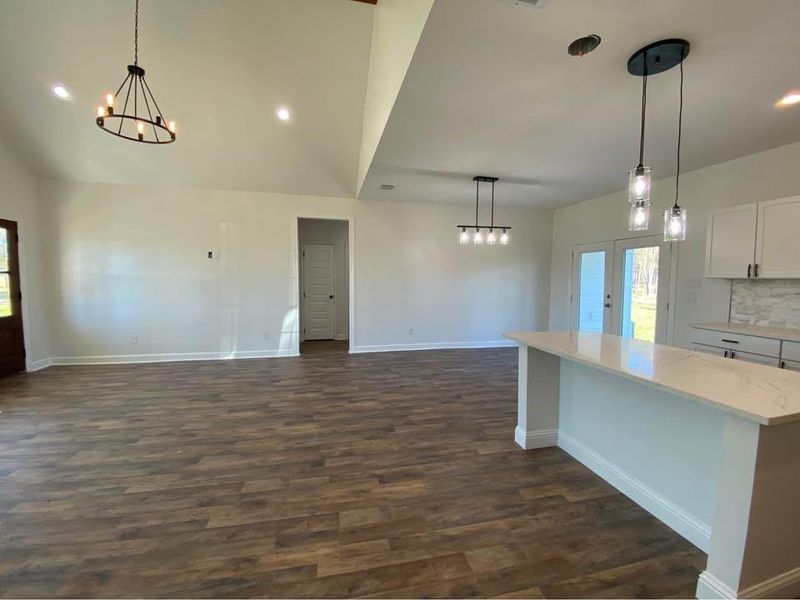 Kitchen featuring dark hardwood / wood-style flooring, backsplash, light stone counters, pendant lighting, and white cabinetry