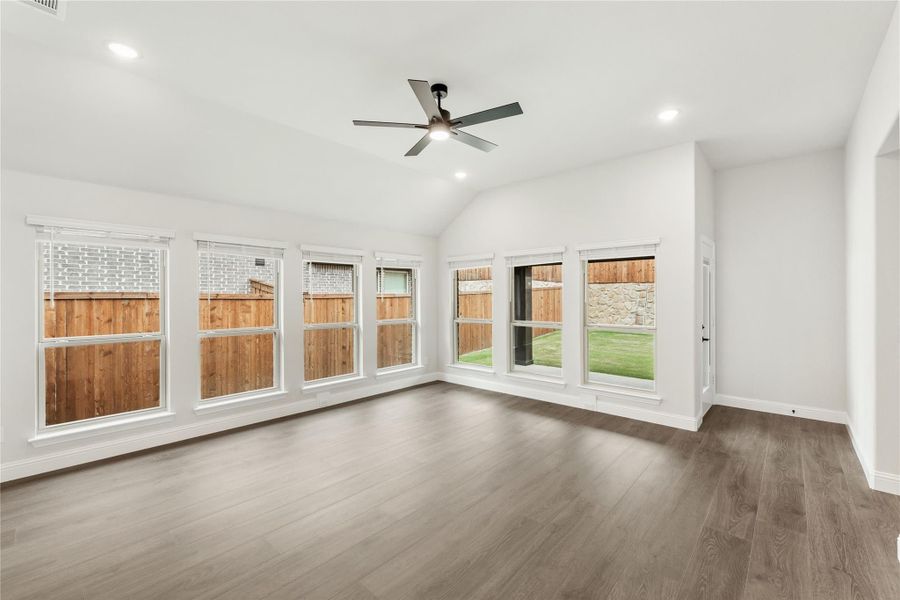 Empty living room with vaulted ceiling, ceiling fan, hardwood floors, and large windows overlooking backyard fence Empty living room with vaulted ceiling, ceiling fan, hardwood floors, and large windows overlooking backyard fence