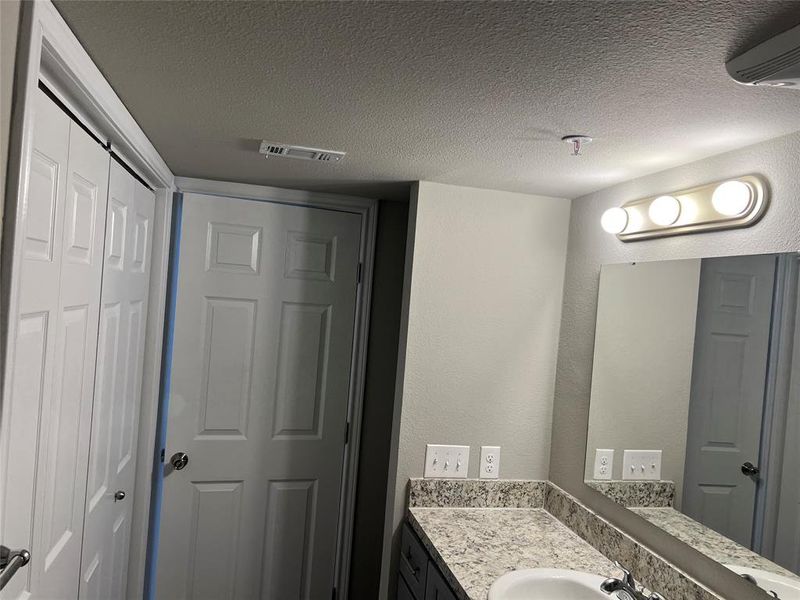 Bathroom with vanity, a textured ceiling, and a wall mounted AC