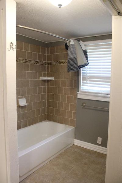 Full bathroom featuring bathing tub / shower combination, light tile patterned flooring, and a textured ceiling Full bathroom featuring bathing tub / shower combination, light tile patterned flooring, and a textured ceiling