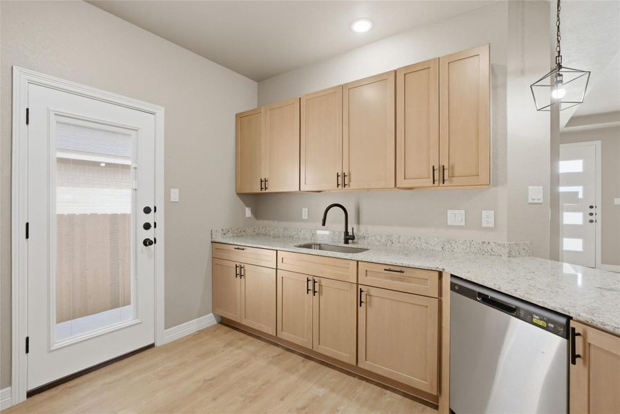 Kitchen with light wood finish cabinetry, light stone countertops, stainless steel dishwasher, and light wood-style flooring