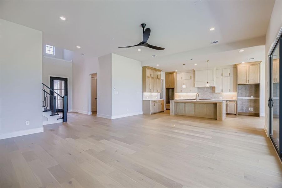 Unfurnished living room with ceiling fan, light wood-style floors, recessed lighting, stairway, and a towering ceiling