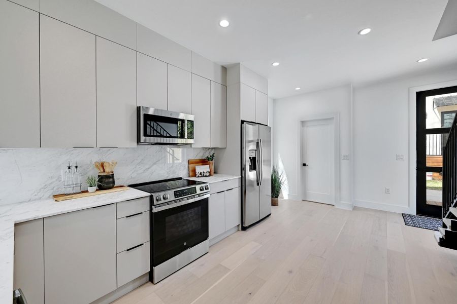 Kitchen with tasteful backsplash, light wood finished floors, light countertops, stainless steel appliances, and modern cabinets