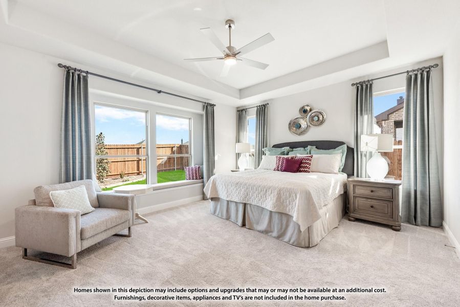 Spacious master bedroom with tray ceiling, ceiling fan, carpet flooring, and large windows overlooking backyard