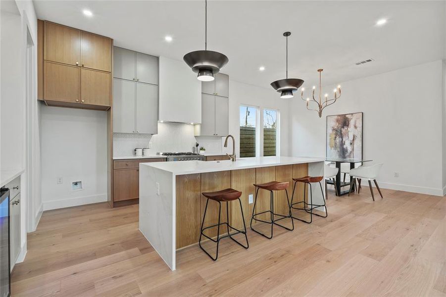 Kitchen featuring brown cabinets, hanging light fixtures, light wood-style floors, a kitchen island with sink, and a breakfast bar