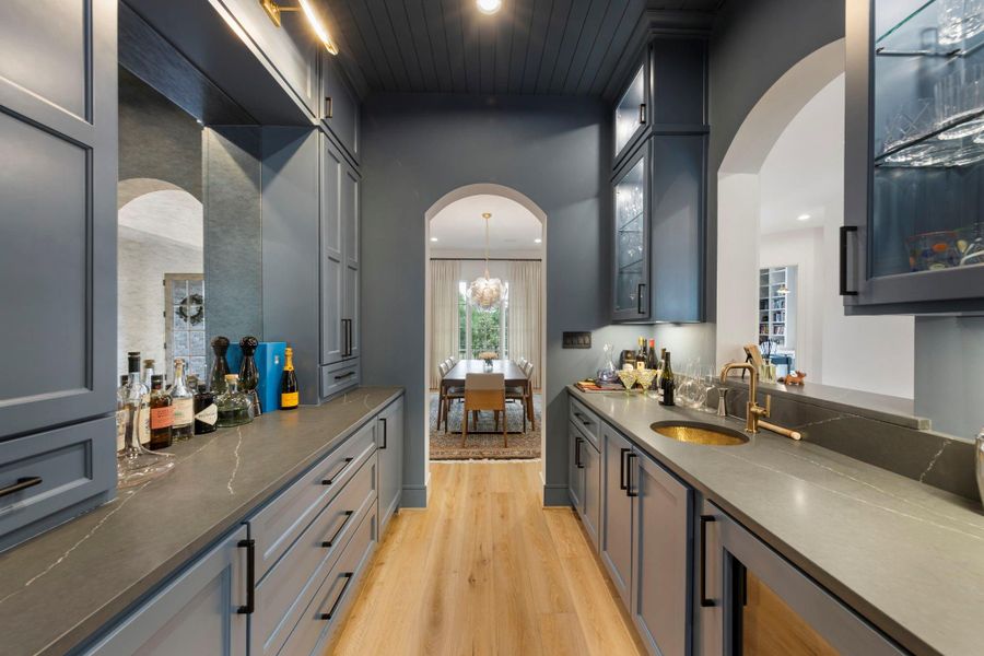 Stylish butler’s pantry and bar featuring custom cabinetry, sleek stone countertops, glass display cabinets, and a designer sink—perfectly positioned for seamless entertaining between the kitchen and dining room.
